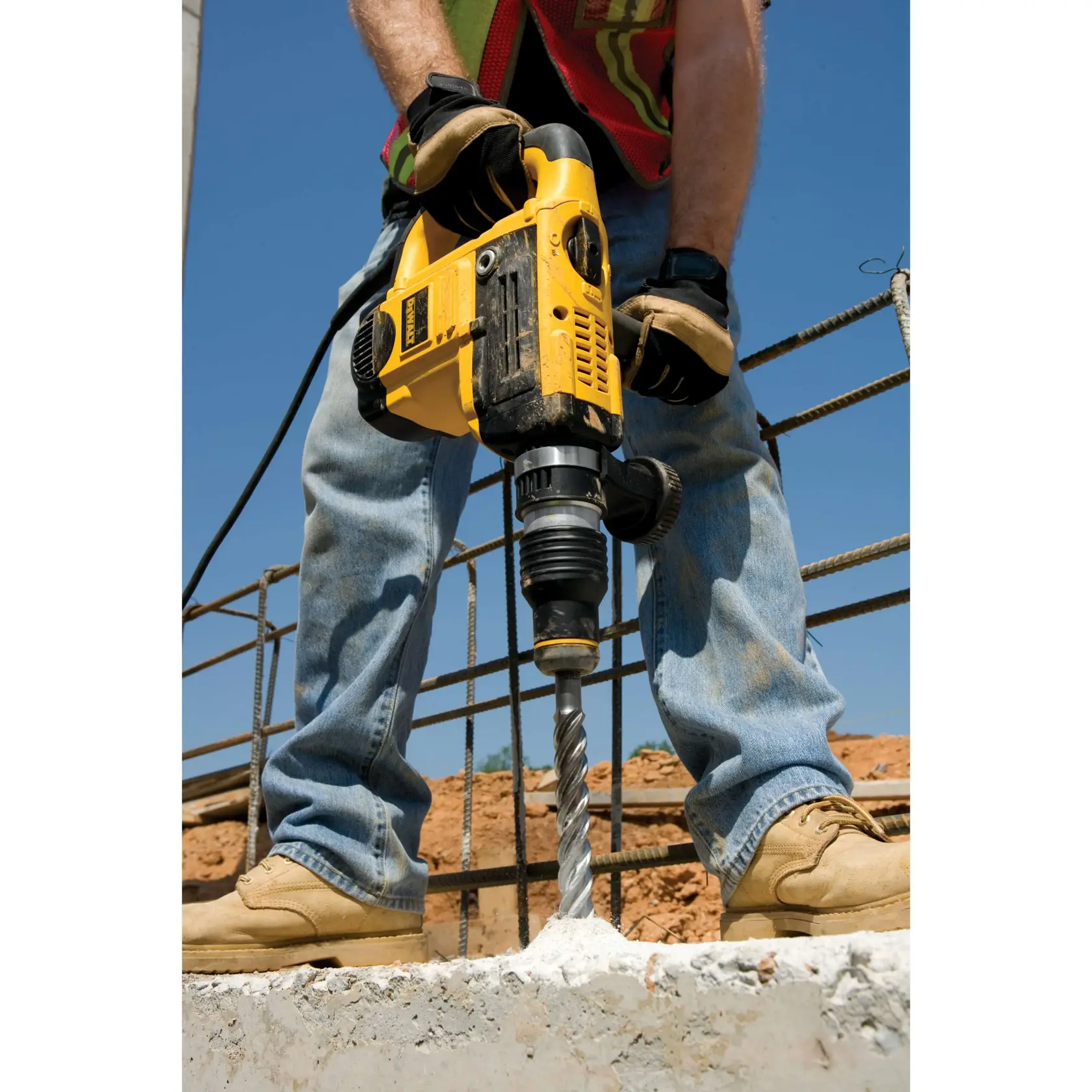 A person wearing safety equipment uses a DEWALT hammer drill (SKU: DT9424) to drill into a concrete wall.