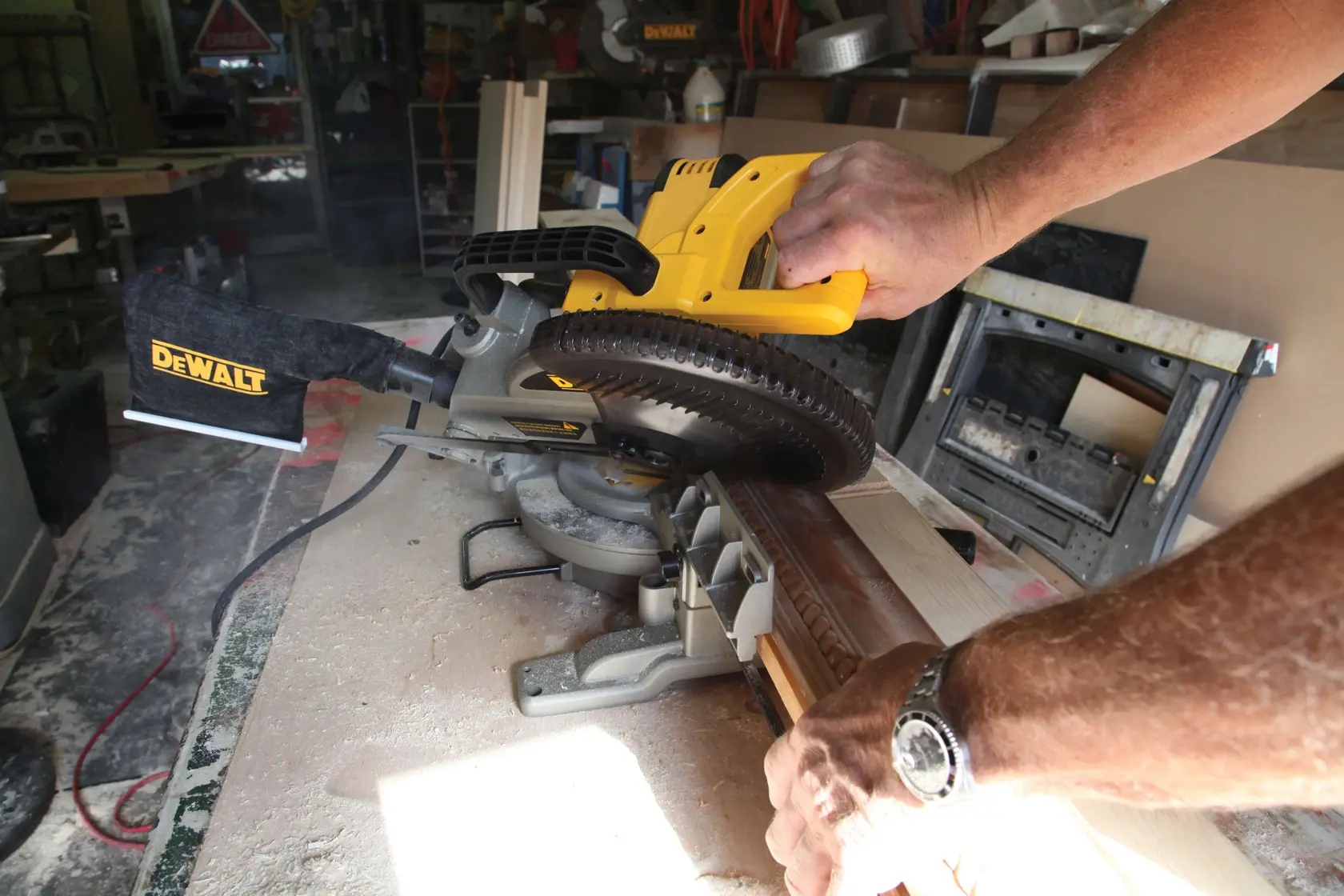 A person uses a DEWALT miter saw to cut a piece of wood in a workshop.