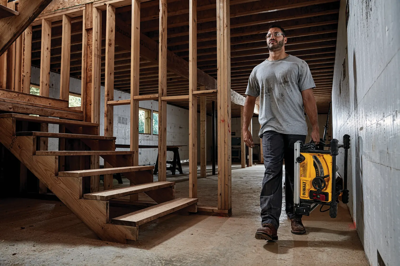 Photo of man carrying DEWALT saw, SKUs DWE7485-GB, DWE7485-QS, DWE7485WS, DWE7485, at construction site.